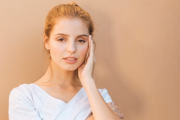 Stressful young woman with her hand on face against beige background