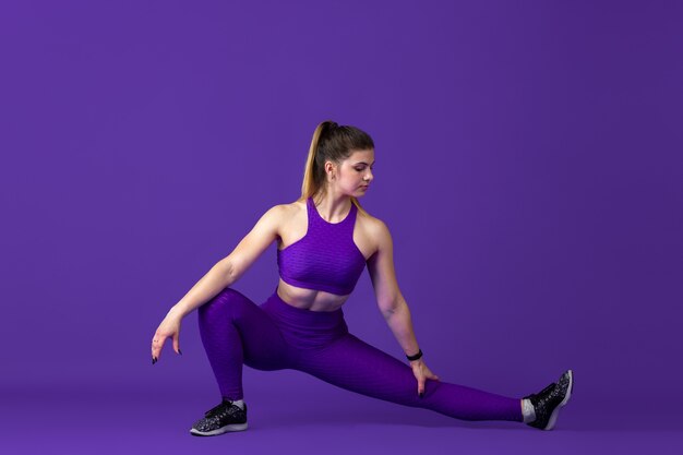 Stretching. Beautiful young female athlete practicing , monochrome purple portrait. Sportive caucasian fit model training. Body building, healthy lifestyle, beauty and action concept.
