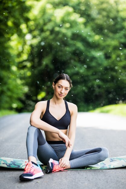Протягивая женщина в упражнениях на открытом воздухе, улыбаясь, делая упражнения йоги, простирается после бега.