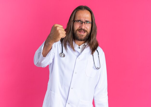 의료 가운과 주먹을 보여주는 안경 청진기를 입고 엄격한 성인 남성 의사