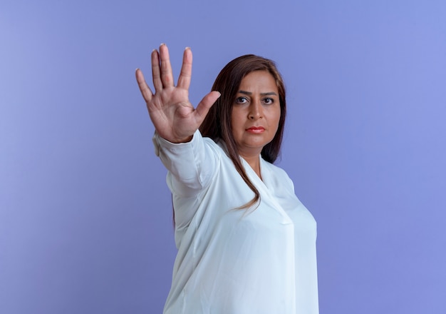 Строгая повседневная кавказская женщина средних лет, показывающая жест стоп на синей стене