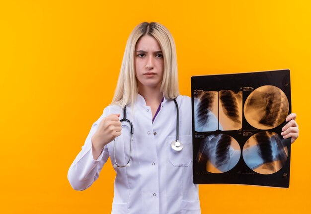 Строгий доктор молодая девушка со стетоскопом в медицинском халате, держащая рентген на изолированном желтом фоне