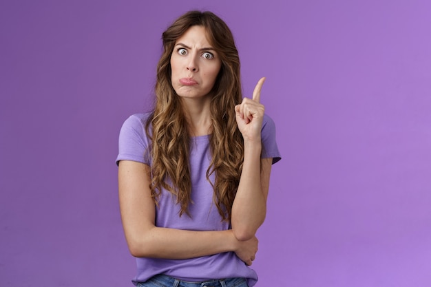 Foto gratuita rigorosa e divertente ragazza dai capelli ricci tirando deluso faccia arrabbiata schioccando gli occhi fissano la macchina fotografica agitando il dito indice disapprovazione rimproverare il cattivo comportamento stare in piedi serio prepotente sfondo viola