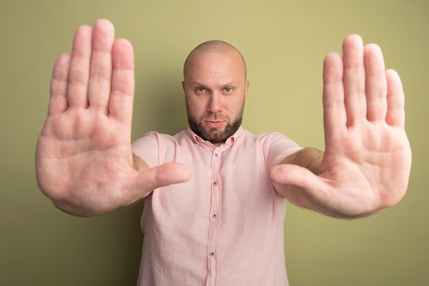 Strict middle-aged bald man wearing pink t-shirt holding hands