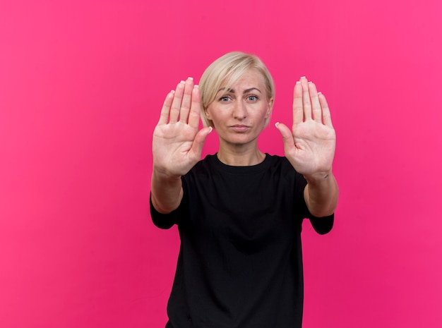 Free photo strict middle-aged blonde slavic woman  doing stop gesture isolated on crimson wall with copy space