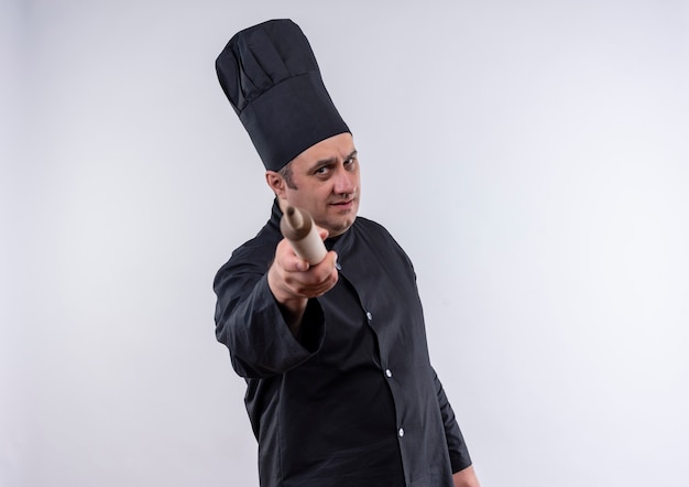 Strict middle-aged male cook in chef uniform holding out to camera rolling pin