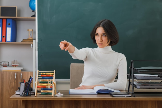 無料写真 教室で学校の道具をつけて机に座っている若い女教師の側の厳しい点