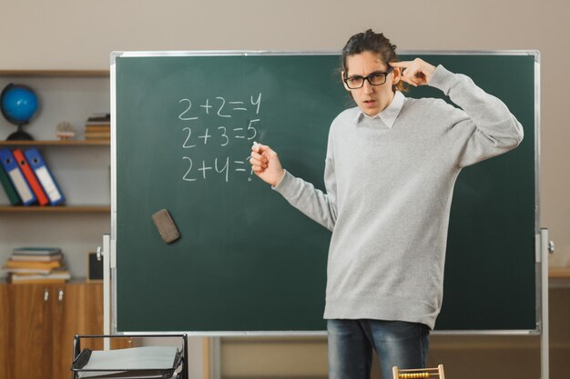 strict putting hand on head young male teacher standing on front of blackboard and write in classroom