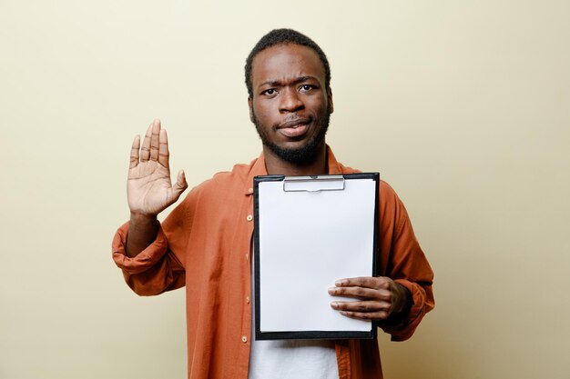 Strict showing stop gesture young african american male holding clipboard isolated on white background