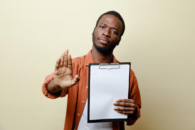 Strict showing stop gesture young african american male holding clipboard isolated on white background