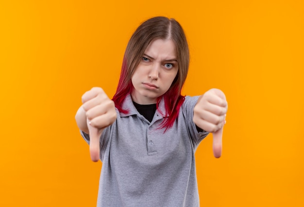 Foto gratuita rigorosa giovane bella ragazza che indossa la maglietta grigia con i pollici in giù su sfondo giallo isolato