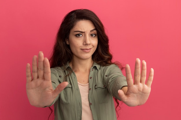 Strict young beautiful girl wearing olive green t-shirt showing stop gesture isolated on pink wall