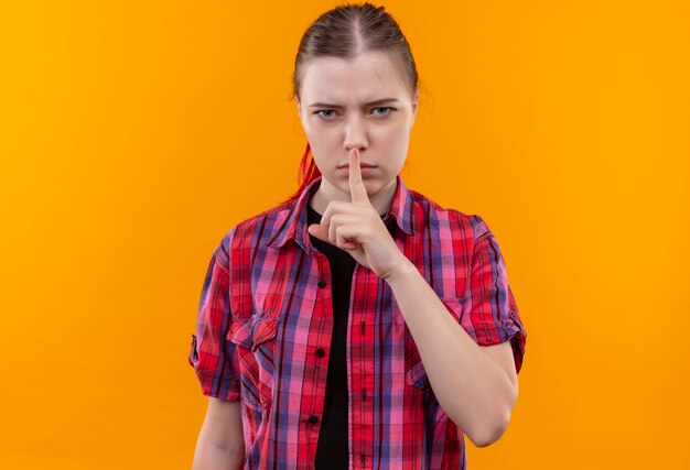 Strict young beautiful girl wearing red shirt showing silence gesture on isolated yellow background with copy space