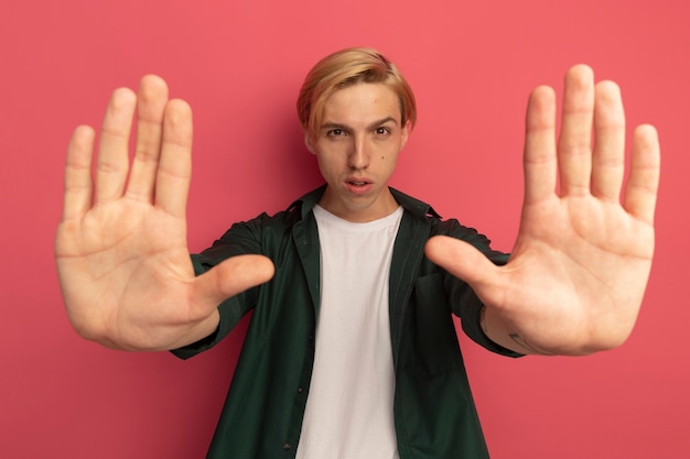 Strict young blonde guy wearing green t-shirt holding out hands