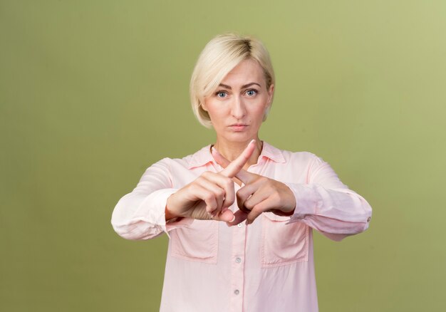 Strict young blonde slavic woman showing gesture of no isolated on olive green