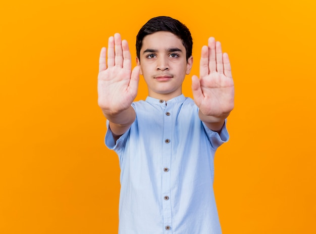 Free photo strict young caucasian boy looking at camera doing stop gesture isolated on orange background with copy space