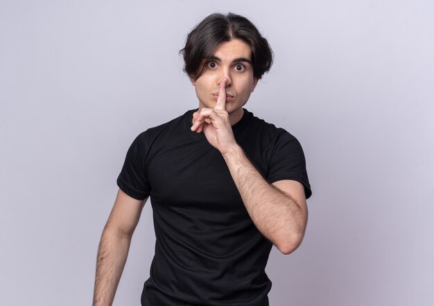 Strict young handsome guy wearing black t-shirt showing silence gesture isolated on white wall