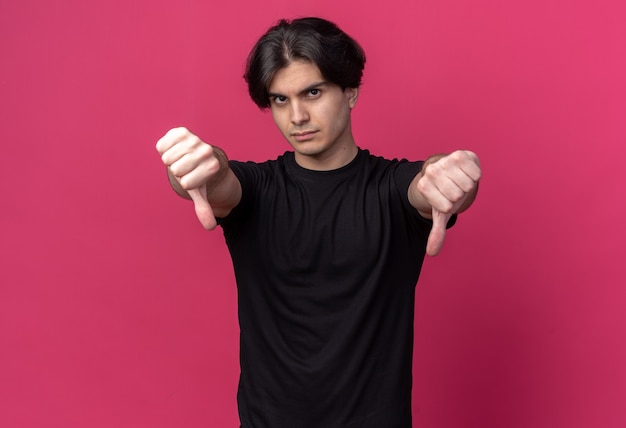 Strict young handsome guy wearing black t-shirt showing thumbs down isolated on pink wall