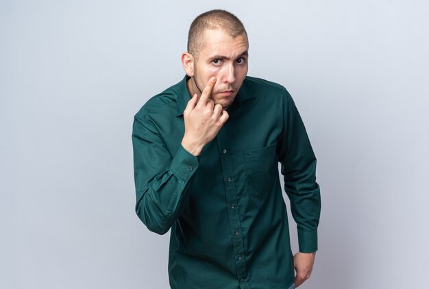 Strict young handsome guy wearing green shirt pulling eye lids 