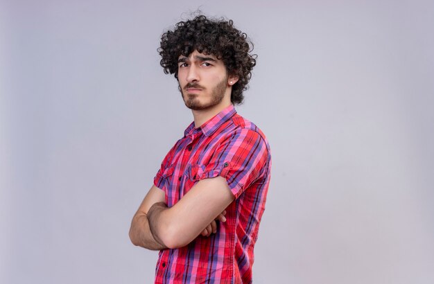 A strict young handsome man with curly hair in checked shirt holding hands folded 