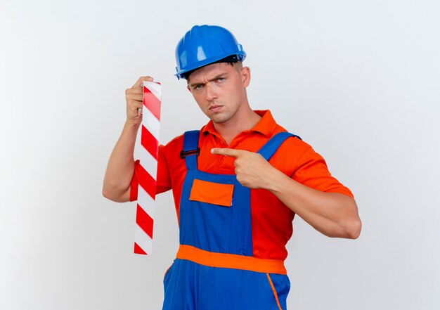 Strict young male builder wearing uniform and safety helmet holding and points at duct tape on white