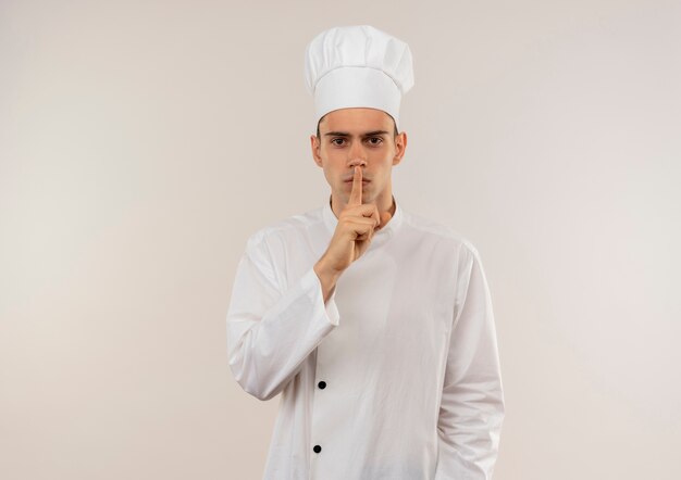 コピースペースで沈黙のジェスチャーを示すシェフの制服を着た厳格な若い男性料理人
