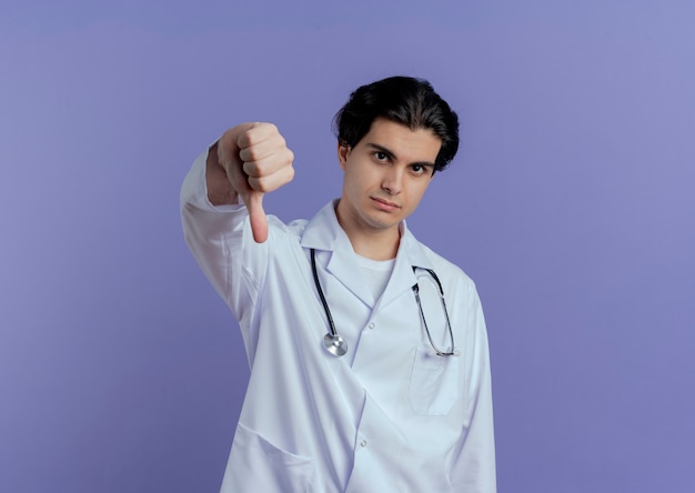 Строгий молодой врач-мужчина в медицинском халате и стетоскопе показывает большой палец вниз на фиолетовой стене с копией пространства