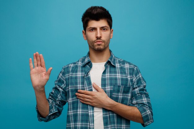Strict young man looking at camera keeping hand on chest showing stop gesture isolated on blue background