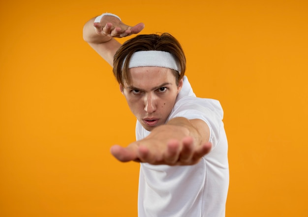 Foto gratuita rigoroso giovane ragazzo sportivo che indossa la fascia e il braccialetto tendendo la mano isolata sulla parete arancione