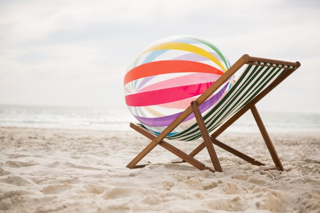 Striped beach ball kept on empty beach chair