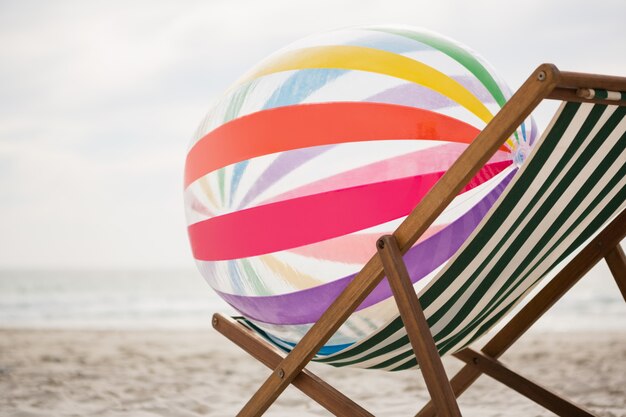 Striped beach ball kept on empty beach chair