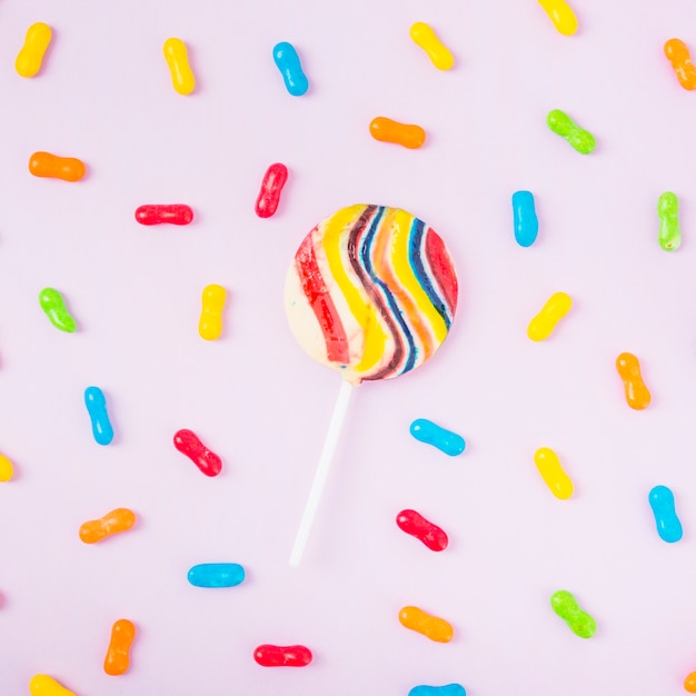 Free photo striped lollipop with colorful candies over the pink backdrop