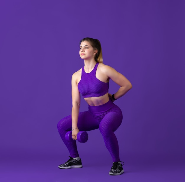 Strong. Beautiful young female athlete practicing in studio, monochrome purple portrait.