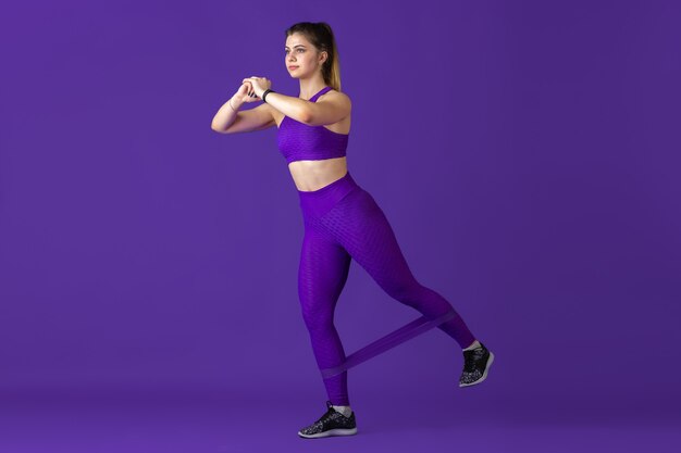 Strong. Beautiful young female athlete practicing in studio, monochrome purple portrait.