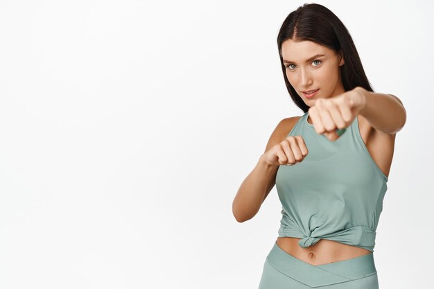 Strong and confident female athlete practice punches stretch out fist while boxing standing in workout clothes over white background