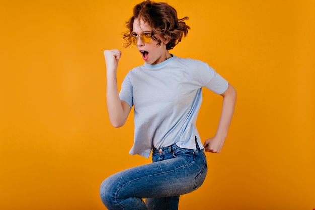 黄色の空間にジャンプする青いTシャツの強い熱狂的な女の子