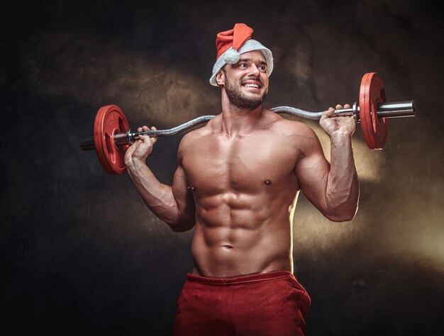 Strong fit man is holding a barbell while posing for photographer in Christmas time.