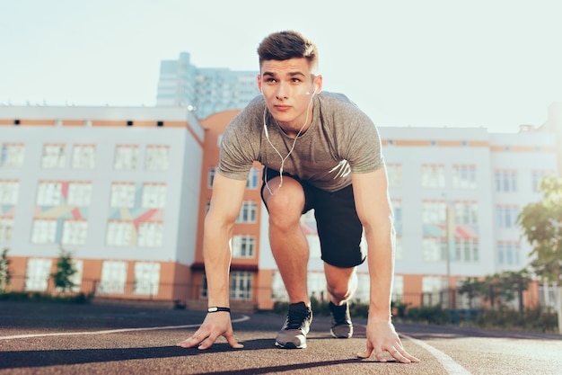 Strong handsome guy in the morning on stadium. He wears sport clothes, listening to music through headphones, has preparation on start.