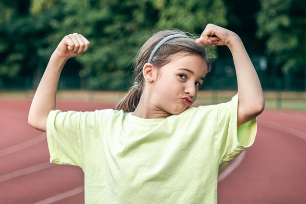 Strong little girl posing outdoors showing their muscles