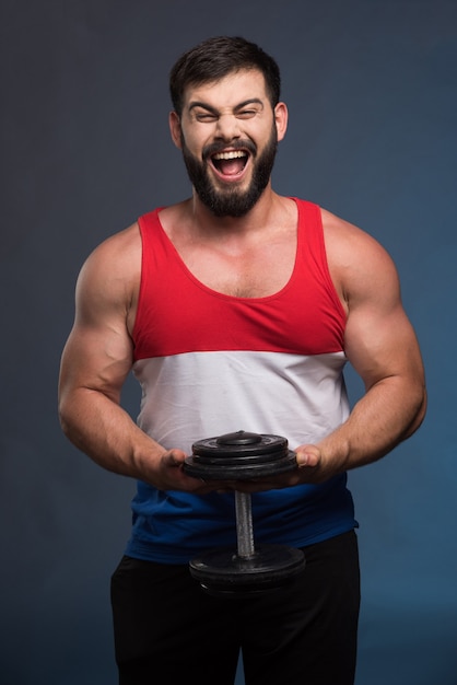 Strong man holding a dumbbell on dark blue wall.