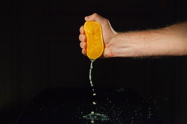 Strong man's hand squeezes half of an orange on glass table