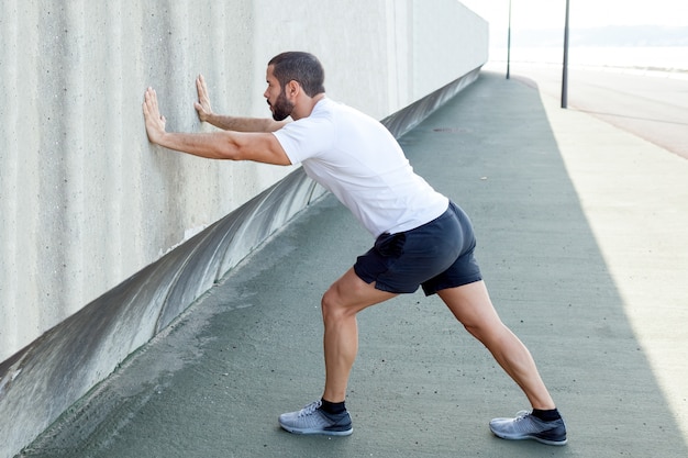 Uomo forte che si allunga vitello e si appoggia sul muro