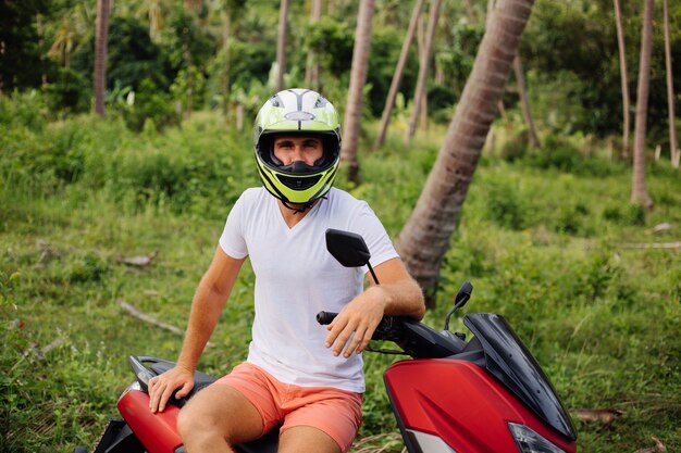 Strong man on tropical jungle field with red motorbike