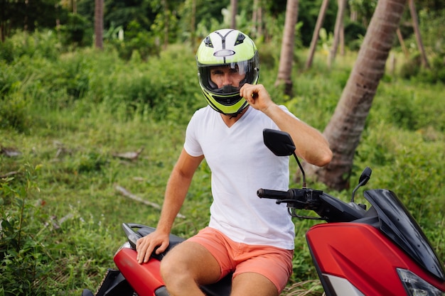 Strong man on tropical jungle field with red motorbike
