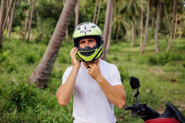Strong man on tropical jungle field with red motorbike