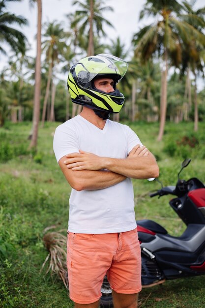 Сильный человек на поле тропических джунглей с красным мотоциклом