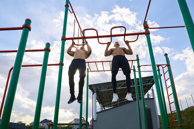 Free photo strong men doing exercises for arms on sports ground