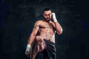 Free photo strong muscular fighter is showing his punch while posing for photographer at dark photo studio.