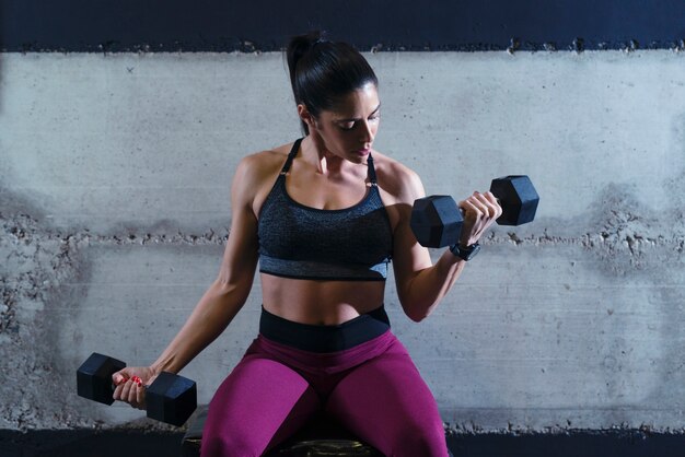 Сильная мускулистая фитнес-женщина, усердно работающая в тренажерном зале, поднимая тяжести и тренируя бицепсы