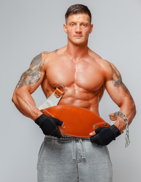 Free photo strong muscular man poses showing his body and holding power belt